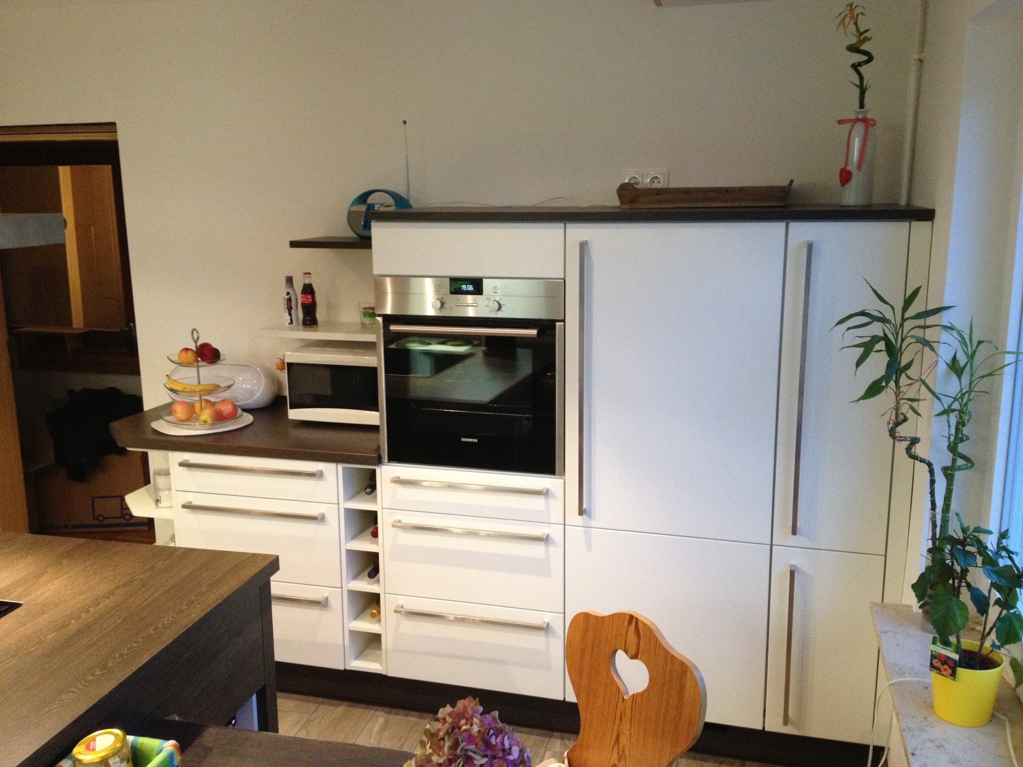 abgeschrägtes Schlussregal, Stangengriffe, weiße Fronten, hochgebauter Backofen, Weinregal