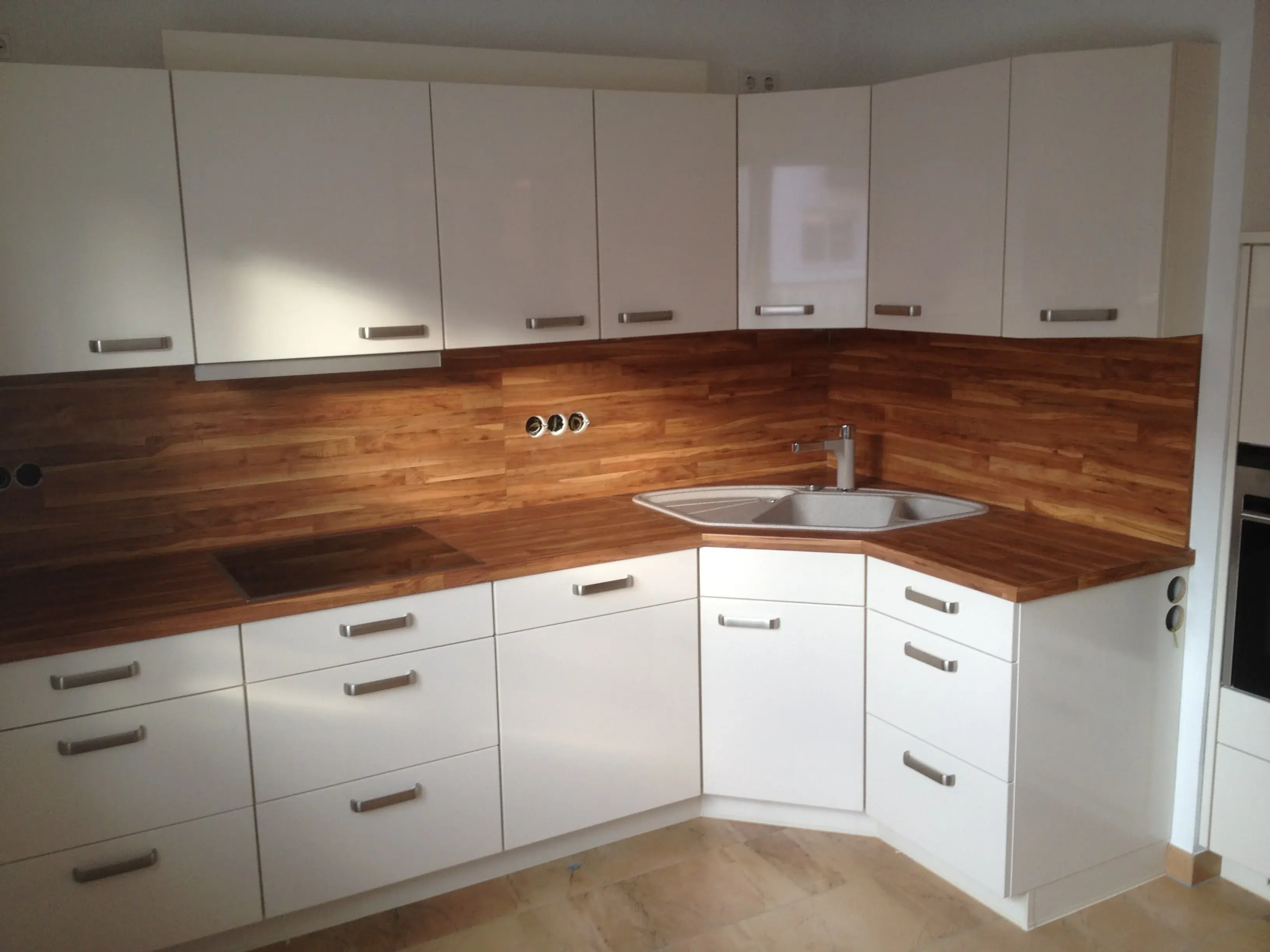 Hochglanzfront mit kräftigem Holzton, Stangengriffe, Hängeschränke, Spülbecken in der Ecke